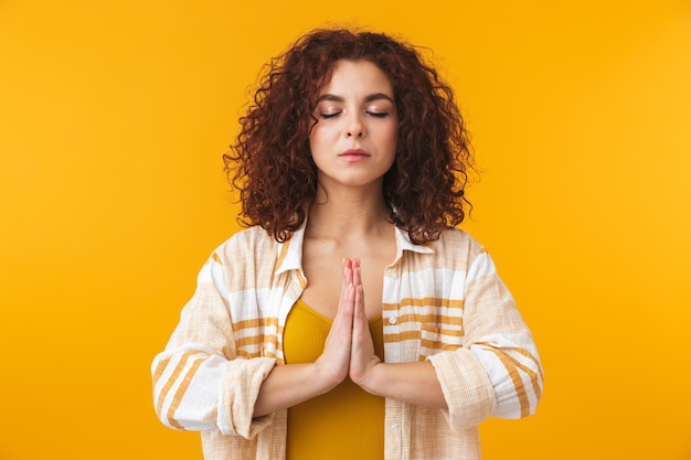Portrait of a beautiful young curly woman posing isolated on yellow wall meditate.