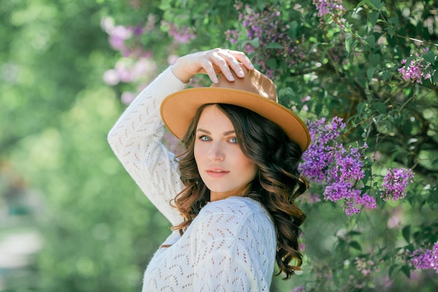 Portrait of beautiful young darkhaired woman with blue eyes in hat near the blooming happy model with curly hair spring