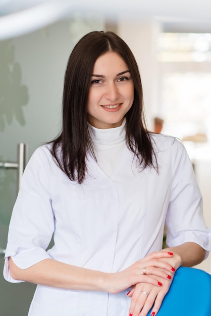 Портрет красивой молодой женщины-стоматолога в ее кабинете, улыбающейся