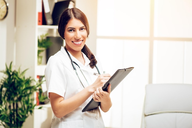 Portrait of a beautiful young female doctor standing in her consulting room, smiling and looking at camera.