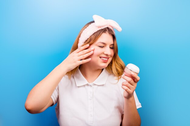 Portrait of beautiful young girl applying some cream to her face for skin care