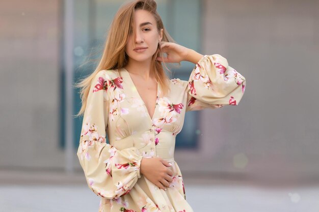 Portrait of a beautiful young girl on a background of a blue business center dressed in a summer beige dress