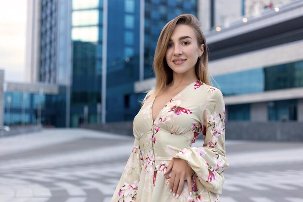 Portrait of a beautiful young girl on a background of a blue business center dressed in a summer beige dress