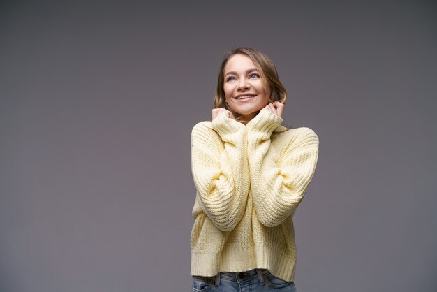 Portrait of a beautiful young girl of caucasian ethnicity in a yellow sweater on a gray background c...