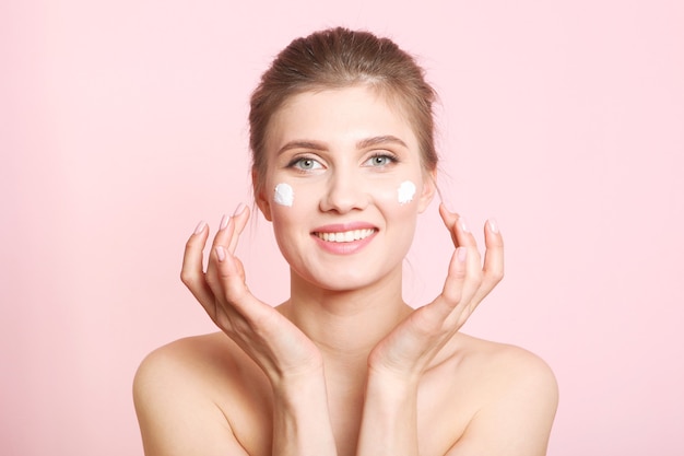 Portrait of a beautiful young girl on a colored background who uses caring cream