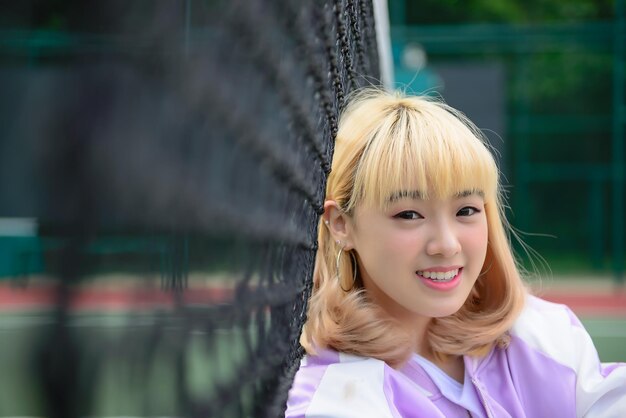 Portrait of beautiful young girl gold hair on the fencePretty woman smiling for take a photo outdoorskawaii style