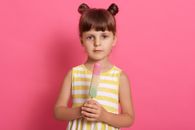 Portrait of a beautiful young girl holding water ice cream and looking directly at camera with sad expression, having knots, wearing summer dress.