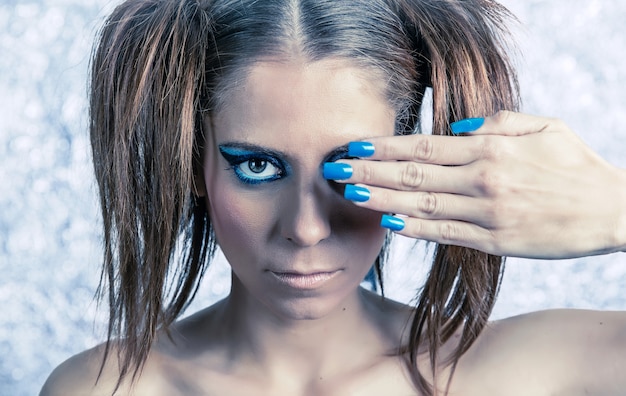 Portrait of beautiful young girl model with pigtails, bright fancy makeup and blue manicure over a blurred metallic background