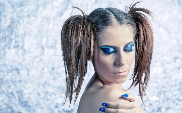 Портрет красивой молодой девушки-модели с косичками, ярким причудливым макияжем и синим маникюром на размытом металлическом фоне