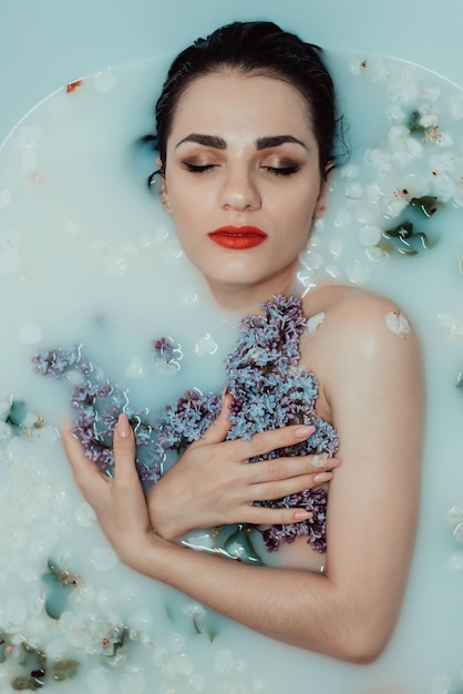 Portrait of a beautiful young girl relaxing and resting in the bath with milk and flowers of lilac