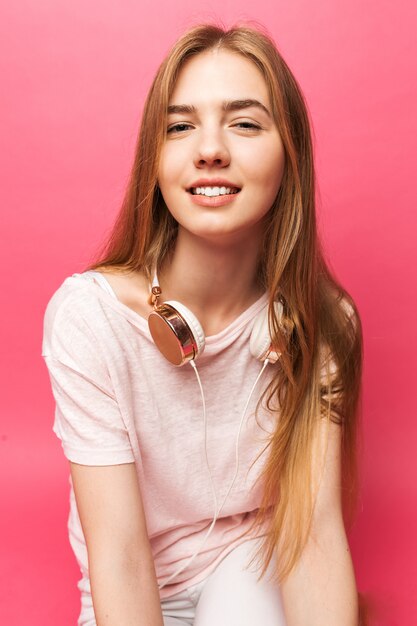 Photo portrait of beautiful young girl standing on pink wall with headphones smiling