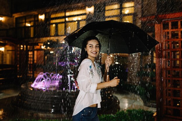 Portrait of beautiful young girl walking with umbrella under rain