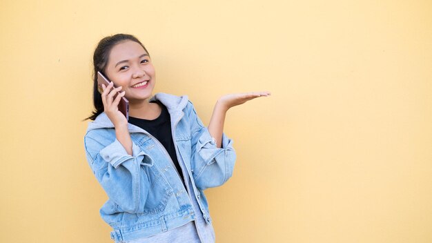 Ritratto di bella ragazza indossare giacca jean parlando con il cellulare su arancione bcakgroundasian ragazza