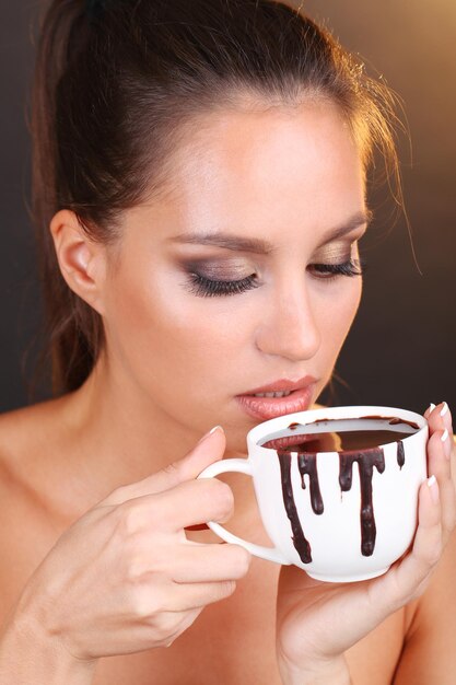 Portrait of beautiful young girl with cup of hot chocolate on brown background