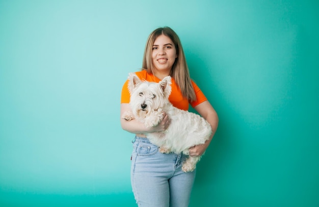 Photo portrait of a beautiful young girl with a dog in her arms on a blue background the girl hugs her pet west highland white terrier copy space