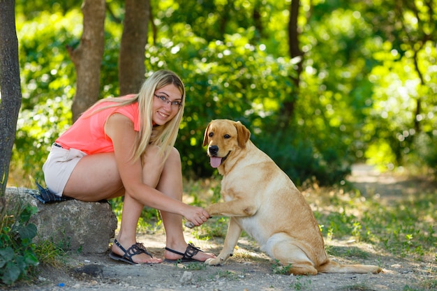 夏の美しい公園で屋外の彼女の犬のラブラドールレトリバーを持つ美しい少女の肖像画