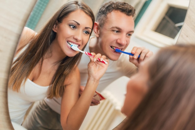 Foto ritratto di una bella giovane coppia felice lavarsi i denti davanti allo specchio del bagno. messa a fuoco selettiva.