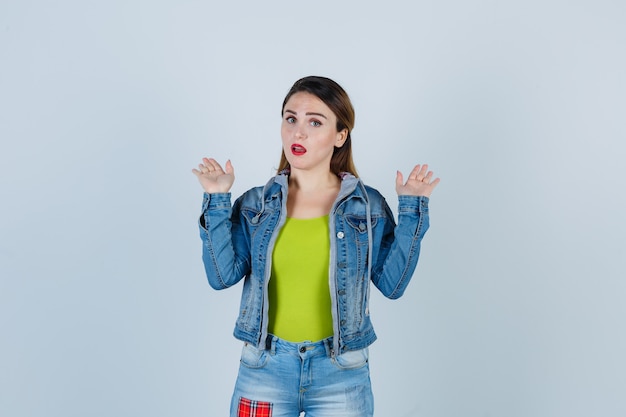 Portrait of beautiful young lady showing surrender gesture in denim outfit and looking puzzled front view