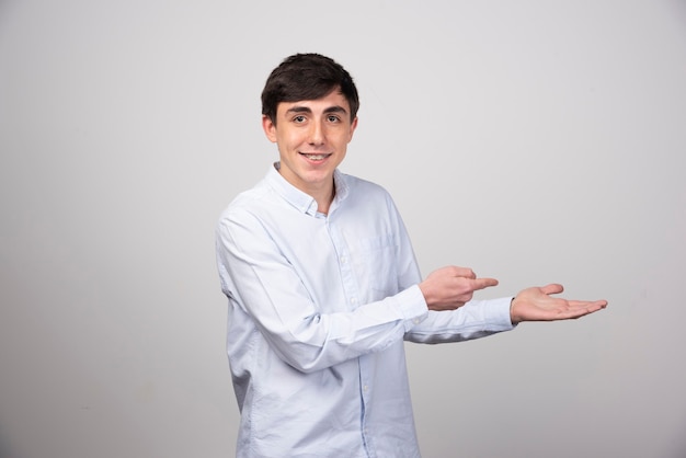 Portrait of beautiful young man holding something on palm and point away side.