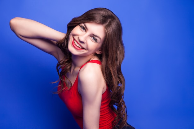 Portrait of beautiful young model in red top and red lips smiling at camera.Isolate.Blue background