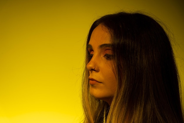 Portrait of beautiful young model with straight hair leaning on a yellow illuminated wall