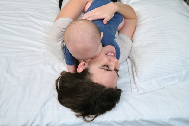 Portrait of beautiful young mother and her baby 7 month old son, parent and baby lying in bed together, view from above