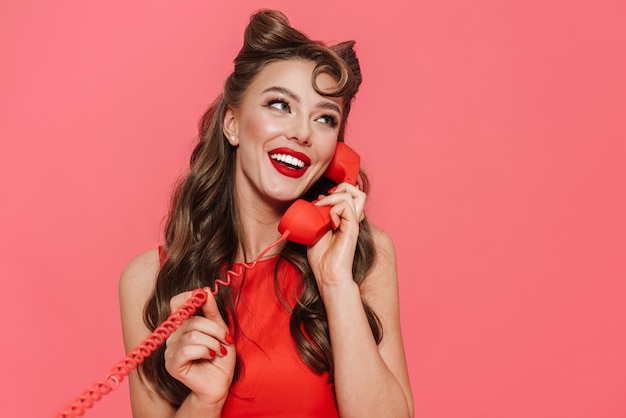 Portrait of a beautiful young pin-up girl wearing dress standing isolated, talking on landline phone