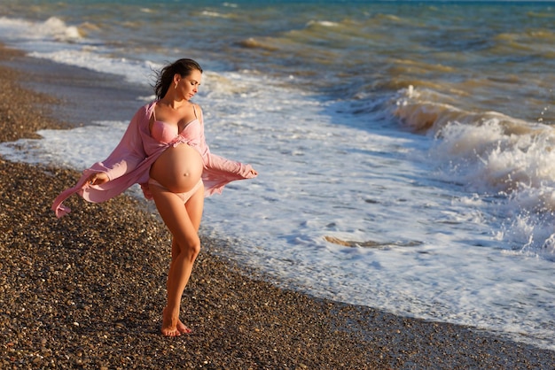 Portrait beautiful young pregnant woman against blue sea on beach thoughtful