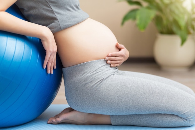 Портрет красивой молодой беременной женщины тренируется с синим фитболом в домашней комнате