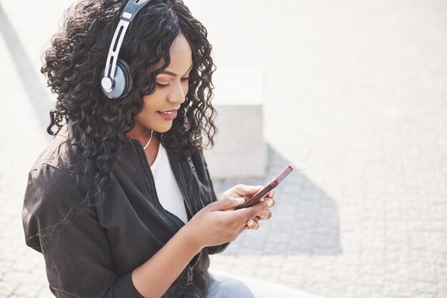 Portrait of a beautiful young pretty African American girl sitting on the beach or lake and listening to music in her headphones