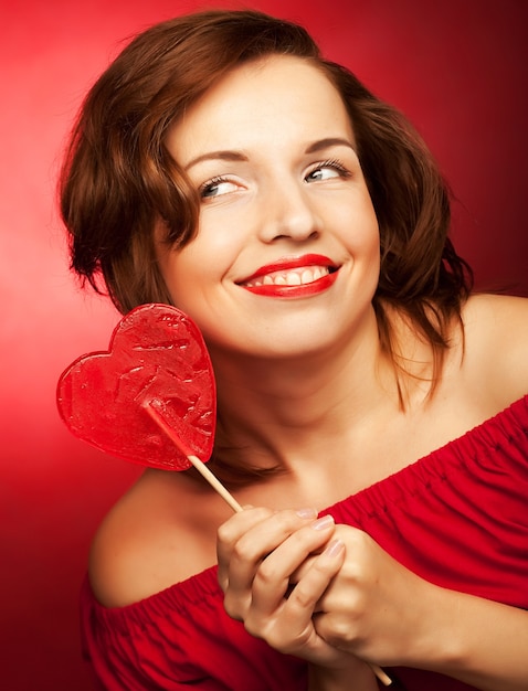 Portrait beautiful young sexy blond girl with red lollipop heart.