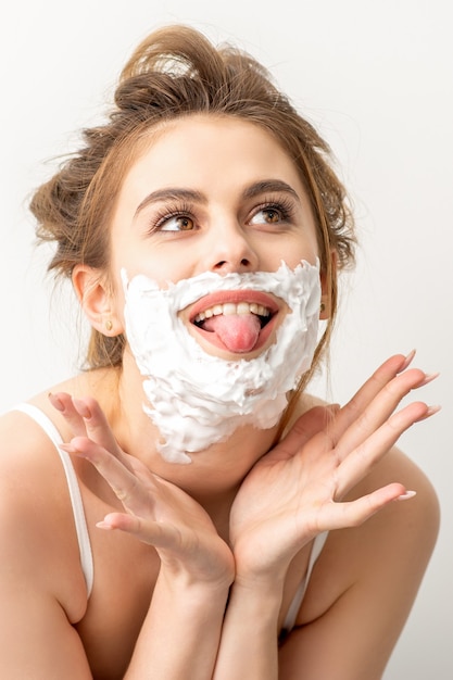 Portrait of a beautiful young smiling caucasian woman posing with shaving foam on the face