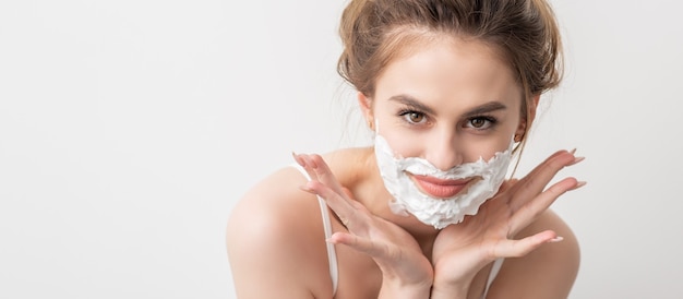 Portrait of a beautiful young smiling caucasian woman with shaving foam on face poses on white backg...