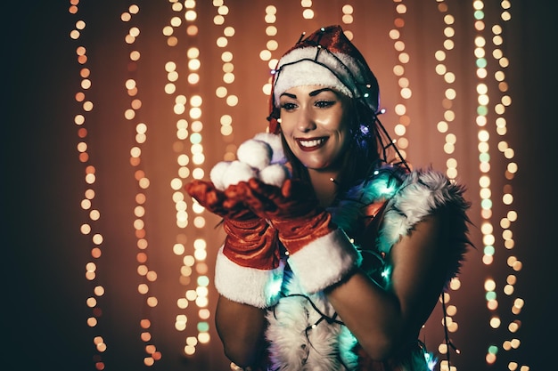 Foto ritratto di una giovane e bella donna sorridente in costume di babbo natale che tiene le palle di neve.
