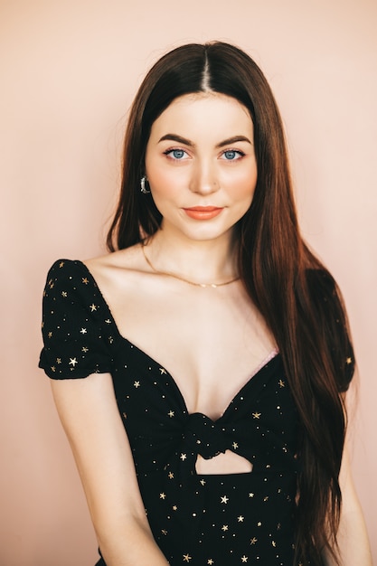 Portrait of beautiful young stylish woman in black dress on beige background