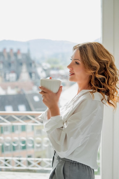 portrait of beautiful young woman 42 years old with cup of hot tea by the window warm cozy home