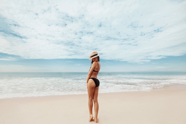 Ritratto bella giovane donna in bikini sulla spiaggia. vista posteriore della ragazza. concetto di libertà, vacanza, spiaggia, sfondo del cielo sereno.