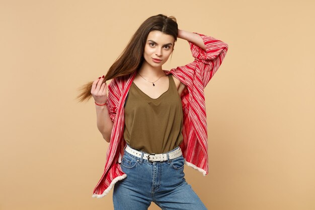 Portrait of beautiful young woman in casual clothes putting hand on head, holding hair isolated on pastel beige background in studio. People sincere emotions, lifestyle concept. Mock up copy space.