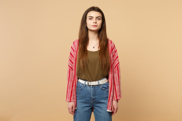 Portrait of beautiful young woman in casual clothes standing and looking camera isolated on pastel beige wall background in studio. People sincere emotions, lifestyle concept. Mock up copy space.