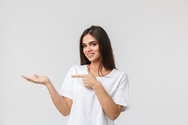 Portrait of a beautiful young woman casualy dressed standing isolated on white, pointing finger at copy space