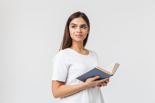 Портрет красивой молодой женщины, повседневно одетой, стоя изолированной на белом, читая книгу