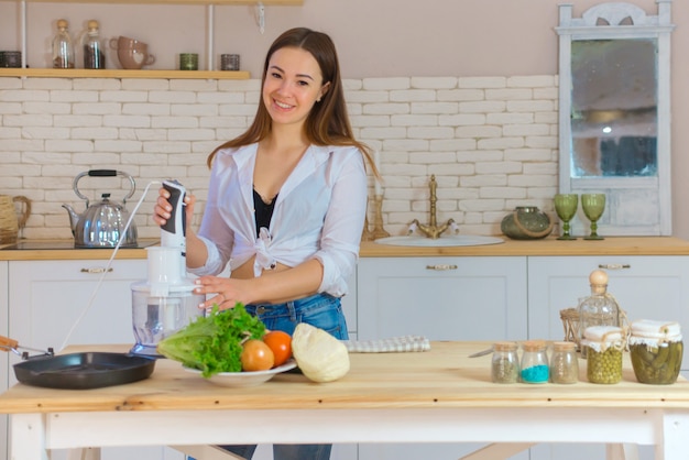 キッチンで料理をしている美しい若い女性の肖像画。若い女性の料理。健康食品-野菜サラダ。