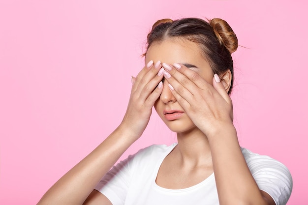 Portrait of beautiful young woman covering her face with her hands on pink background
