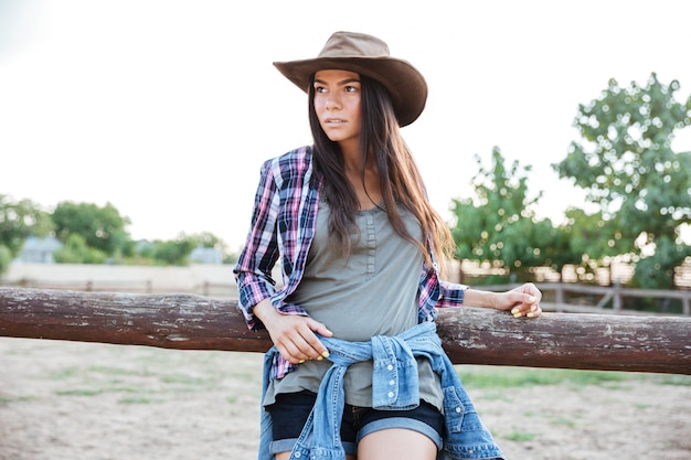 Photo portrait of beautiful young woman cowgirl in hat and checkered shirt