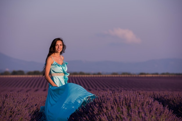 portrait of a beautiful young woman in cyand dress relaxing and having fun on wind at purple lavander flower field