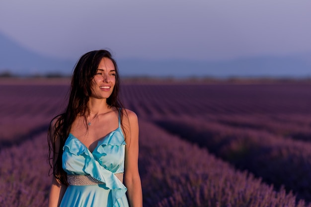 紫色のラベンダーの花畑でリラックスして風に乗って楽しんでいるシアンのドレスを着た美しい若い女性のポートレート