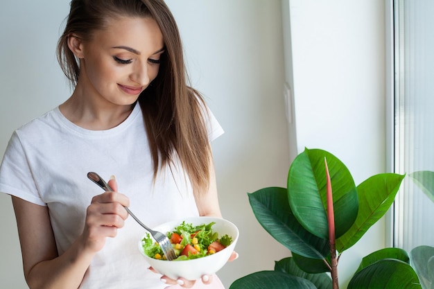 家でダイエット サラダを食べる美しい若い女性の肖像画