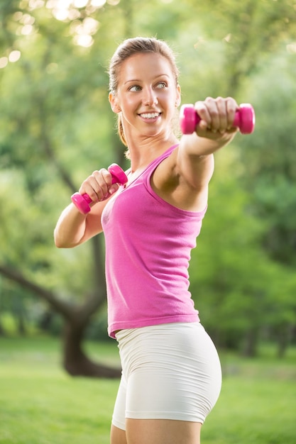 公園でウェイト運動をしている美しい若い女性の肖像画。