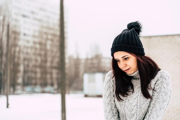 Portrait of a beautiful young woman in a gray knitted sweater standing outdoors during winter