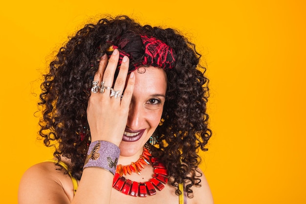 Photo portrait of beautiful young woman in gypsy style standing on yellow background isolated covering one eye with hand.